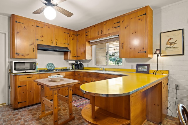 kitchen with gas cooktop, stainless steel microwave, a peninsula, under cabinet range hood, and brick patterned floor
