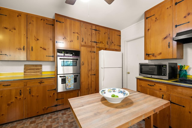 kitchen with stainless steel appliances, brick patterned floor, brown cabinetry, and ceiling fan
