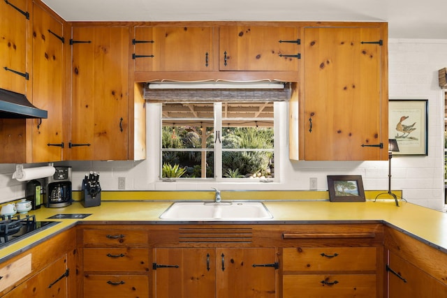kitchen featuring light countertops, under cabinet range hood, a sink, and brown cabinets