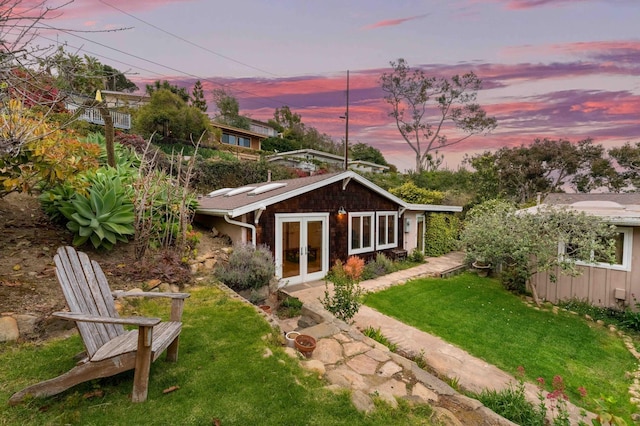 back of property at dusk featuring a lawn, french doors, and solar panels