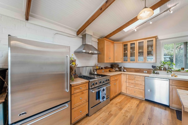 kitchen featuring light wood-style flooring, lofted ceiling with beams, stainless steel appliances, light countertops, and wall chimney exhaust hood