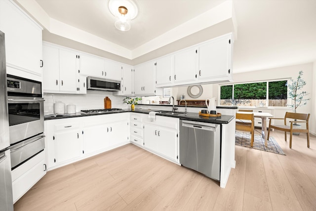 kitchen with a sink, dark countertops, a warming drawer, light wood finished floors, and stainless steel appliances