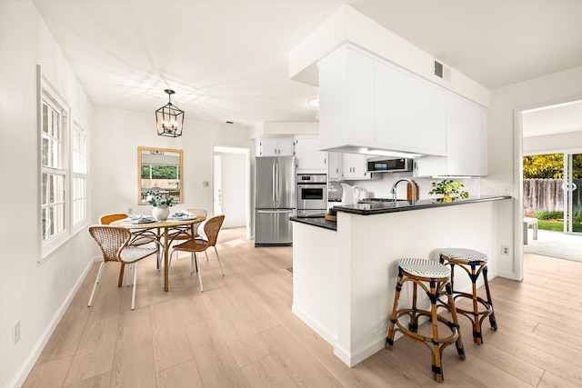 kitchen with white cabinets, light wood-style flooring, appliances with stainless steel finishes, and a peninsula