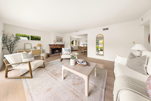 living room with visible vents, a brick fireplace, and wood finished floors