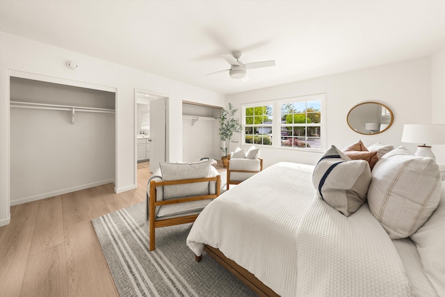 bedroom with ensuite bathroom, baseboards, ceiling fan, light wood-style floors, and multiple closets