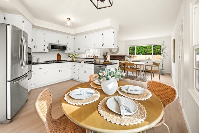 kitchen featuring white cabinetry, dark countertops, light wood-style floors, stainless steel appliances, and a sink