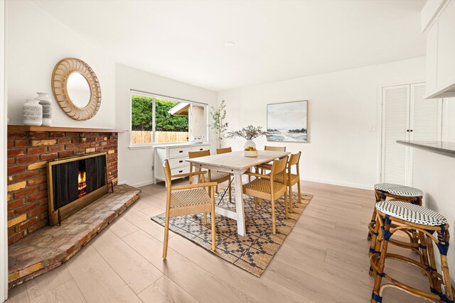dining area featuring light wood finished floors, a brick fireplace, and baseboards