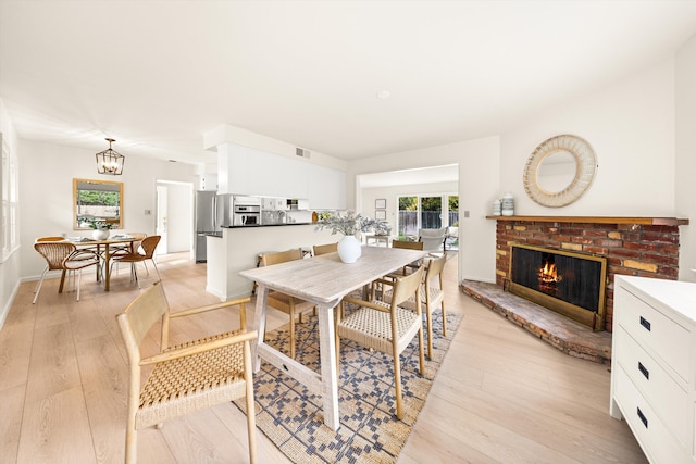 dining space with light wood-style floors, an inviting chandelier, visible vents, and a brick fireplace