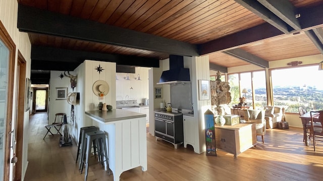 2852 Tapadero Rd, Solvang, CA 93463 - kitchen with wall chimney range hood, wood finished floors, beamed ceiling, a peninsula, and white cabinetry