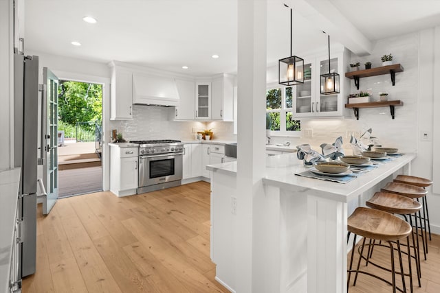 kitchen featuring stainless steel appliances, a peninsula, custom exhaust hood, light wood-style floors, and a breakfast bar