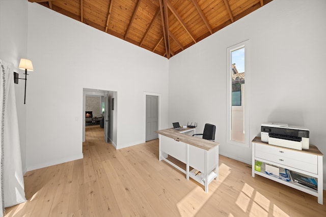 office space featuring light wood finished floors, baseboards, beamed ceiling, wood ceiling, and high vaulted ceiling