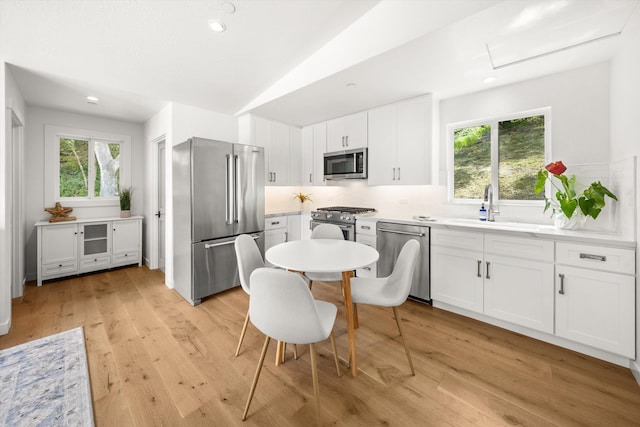 kitchen with stainless steel appliances, backsplash, a sink, light wood-style flooring, and white cabinetry