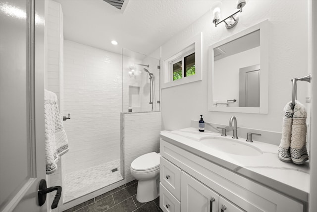 bathroom with visible vents, tiled shower, vanity, and toilet