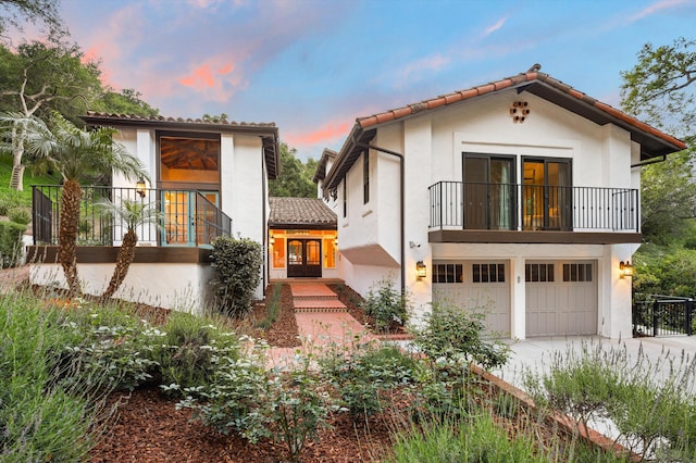 mediterranean / spanish-style home featuring a garage, a balcony, concrete driveway, and stucco siding