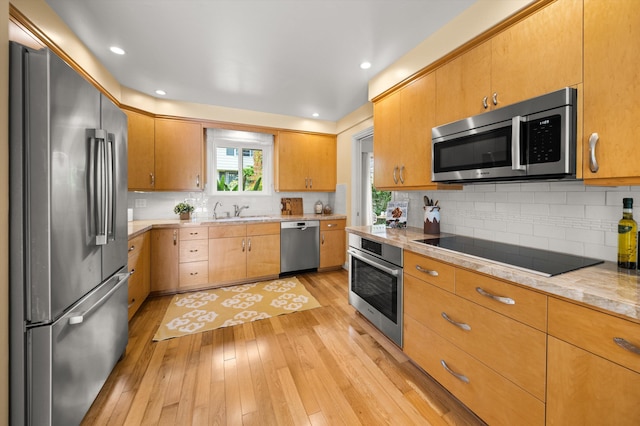 kitchen featuring light countertops, tasteful backsplash, a sink, light wood-style flooring, and appliances with stainless steel finishes