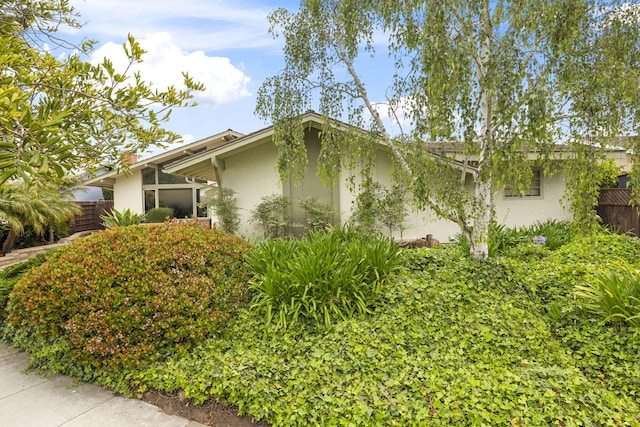 view of side of home with stucco siding and fence