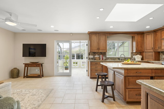 kitchen featuring tasteful backsplash, recessed lighting, a skylight, ceiling fan, and brown cabinetry