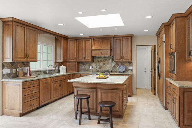 kitchen featuring brown cabinetry, a skylight, a center island, and a sink