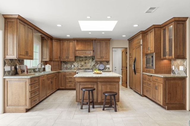 kitchen featuring a skylight, backsplash, a sink, and stainless steel microwave