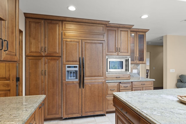kitchen with brown cabinetry, light stone countertops, and built in appliances
