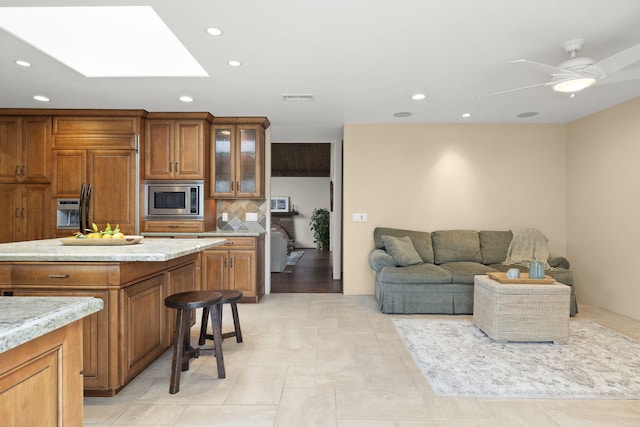 kitchen featuring recessed lighting, visible vents, stainless steel microwave, a skylight, and brown cabinetry