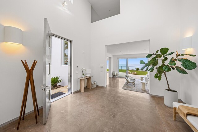 foyer featuring baseboards, a towering ceiling, finished concrete flooring, and a water view