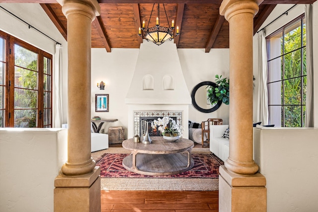 living area with ornate columns, beam ceiling, wooden ceiling, and wood finished floors
