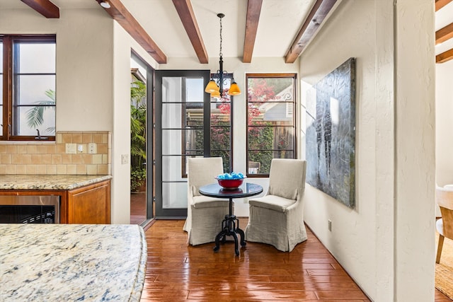 dining space with a notable chandelier, a healthy amount of sunlight, beam ceiling, and hardwood / wood-style floors