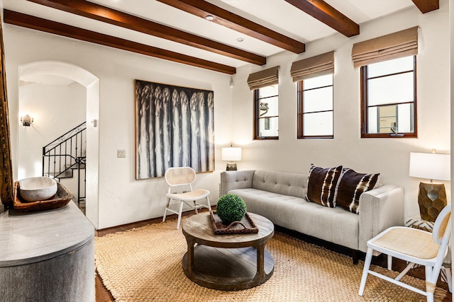 living area featuring stairway, arched walkways, beam ceiling, and baseboards