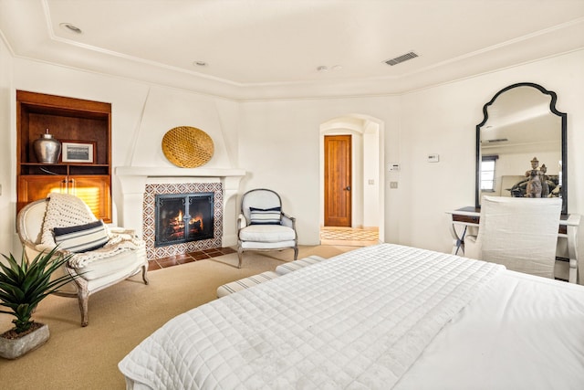 bedroom featuring crown molding, arched walkways, a tile fireplace, carpet, and visible vents
