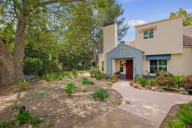 view of front of house featuring stucco siding, a chimney, and a tiled roof