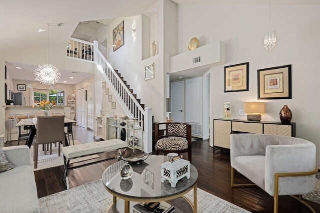 living room with hardwood / wood-style floors, visible vents, stairs, high vaulted ceiling, and a notable chandelier