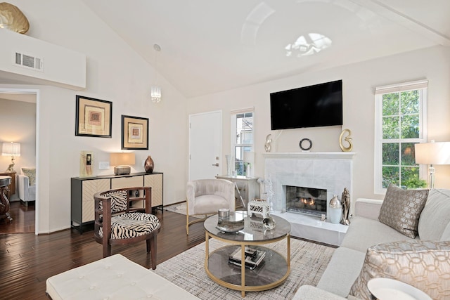 living room with wood finished floors, visible vents, a tile fireplace, and high vaulted ceiling
