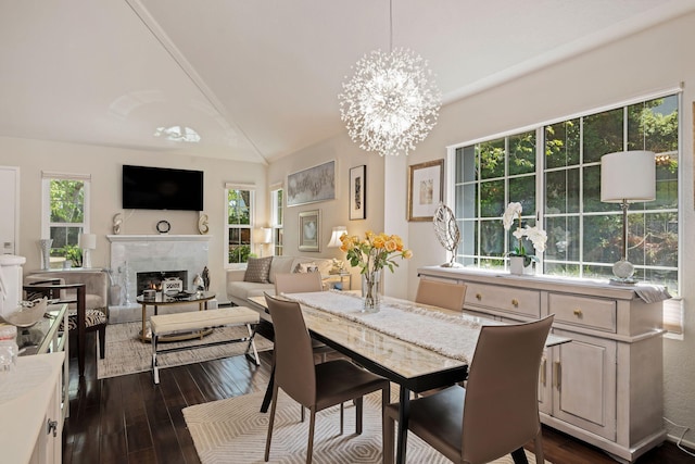 dining space with vaulted ceiling, an inviting chandelier, a lit fireplace, and dark wood finished floors