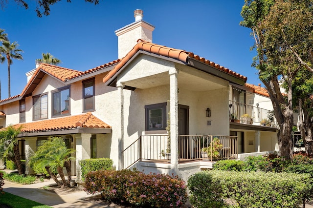 rear view of house featuring a chimney, a tiled roof, and stucco siding