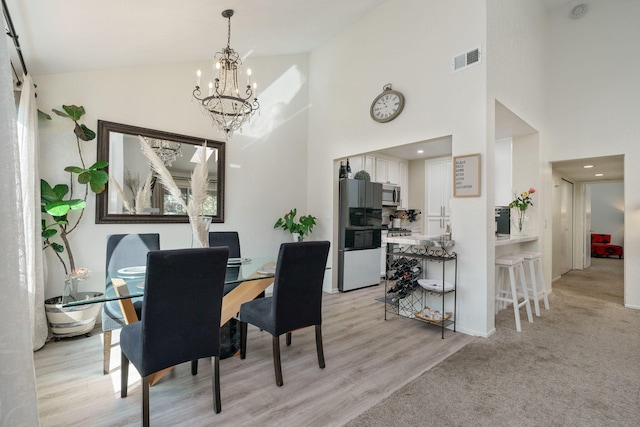 dining room with a chandelier, visible vents, light wood finished floors, and high vaulted ceiling