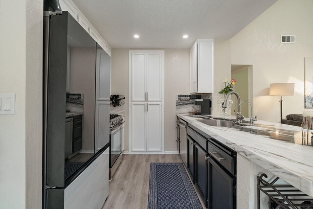 kitchen with white cabinets, stainless steel appliances, light wood-style flooring, a sink, and light stone counters