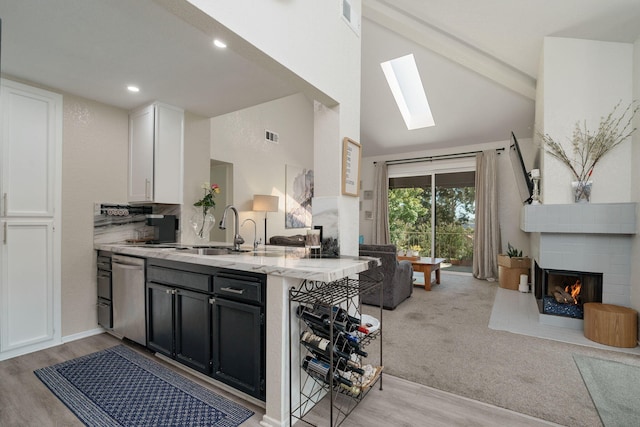 kitchen with stainless steel dishwasher, a sink, a multi sided fireplace, a skylight, and light stone countertops
