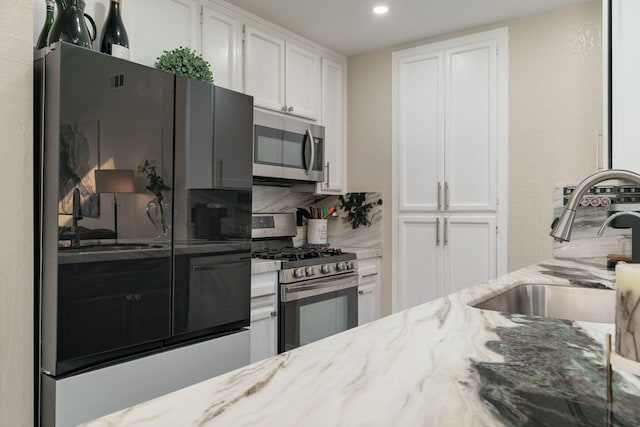 kitchen featuring white cabinets, decorative backsplash, stainless steel appliances, and a sink