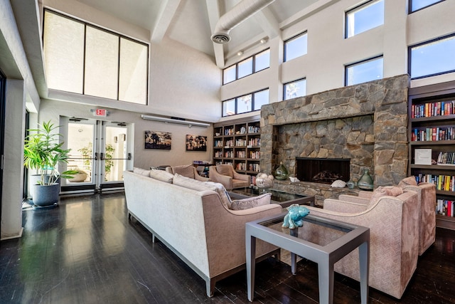 living room with a stone fireplace, a towering ceiling, hardwood / wood-style flooring, and a healthy amount of sunlight