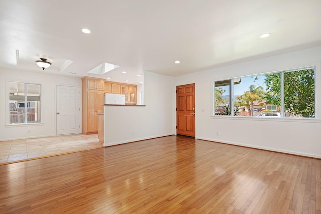 unfurnished living room featuring a skylight, baseboards, recessed lighting, and light wood-type flooring