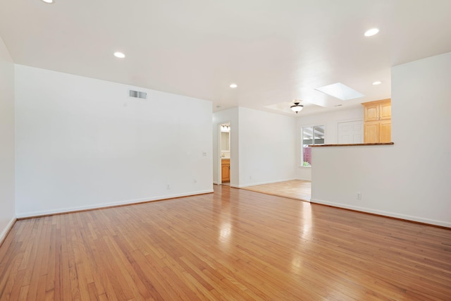 unfurnished living room featuring light wood-style floors, visible vents, a skylight, and baseboards