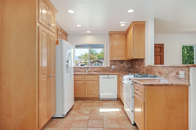 kitchen with a peninsula, light brown cabinetry, and white appliances