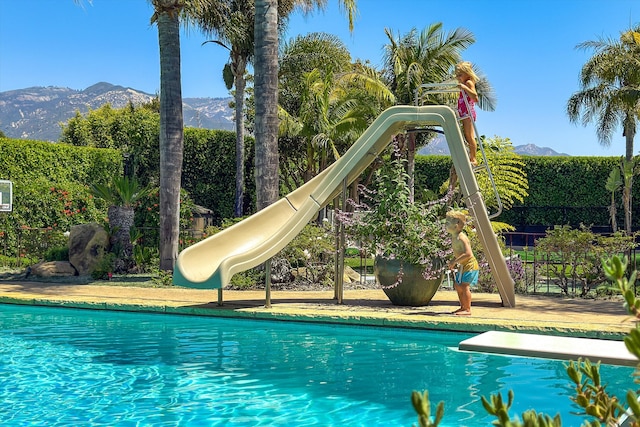 view of swimming pool with a diving board, a water slide, and a mountain view