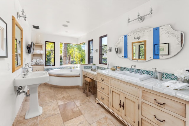 bathroom featuring visible vents, two sinks, a bath, and stone tile flooring