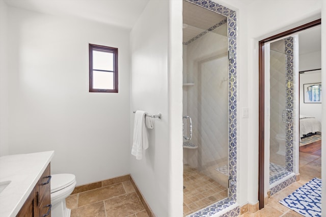 bathroom with a shower stall, vanity, baseboards, toilet, and stone tile floors