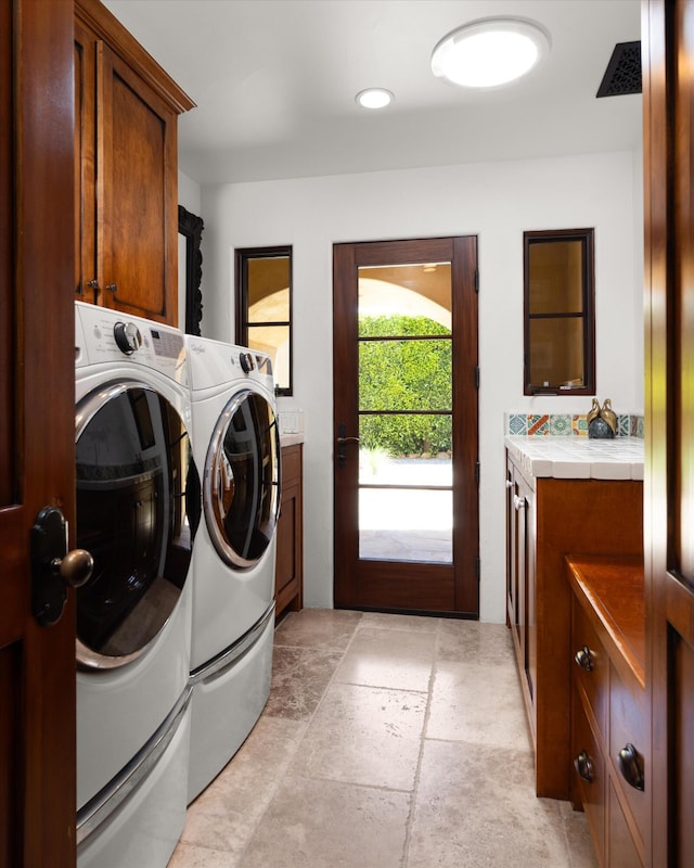 washroom featuring stone finish floor, cabinet space, and washer and clothes dryer