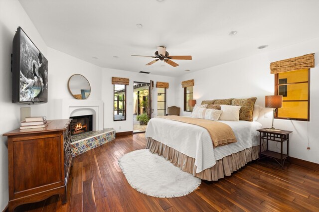 bedroom featuring access to outside, a warm lit fireplace, baseboards, and dark wood-type flooring