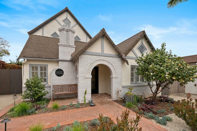 tudor-style house featuring stone siding, stucco siding, and fence