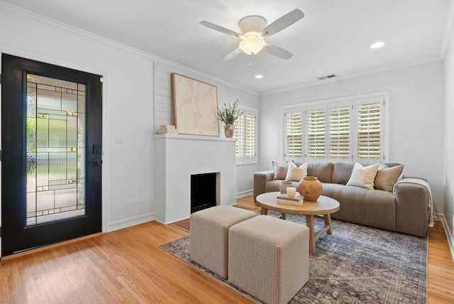living room featuring a fireplace with flush hearth, wood finished floors, visible vents, and crown molding